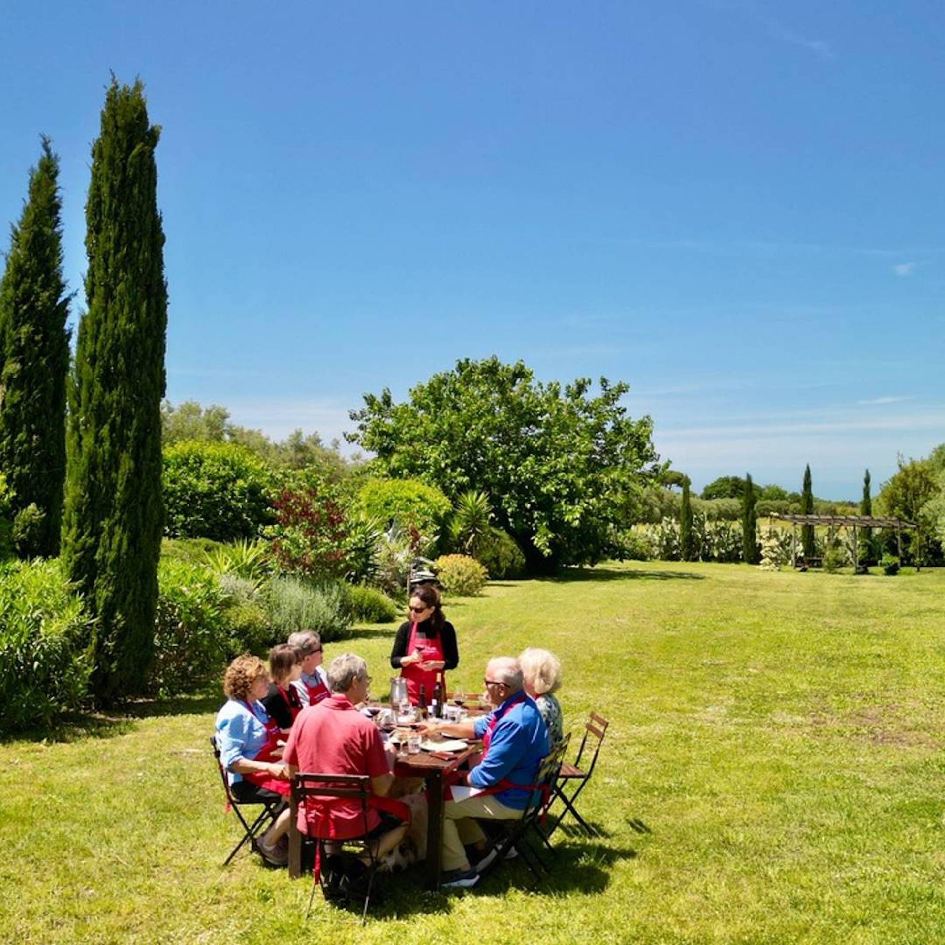 Cooking in Tuscany guests enjoy an outdoor garden lunch under a bright blue sky at Chicca’s Tuscan farmhouse.