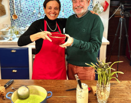 Chicca and Giuliano Hazan smile in the Tuscan farmhouse kitchen while holding a bowl of asparagus soup.