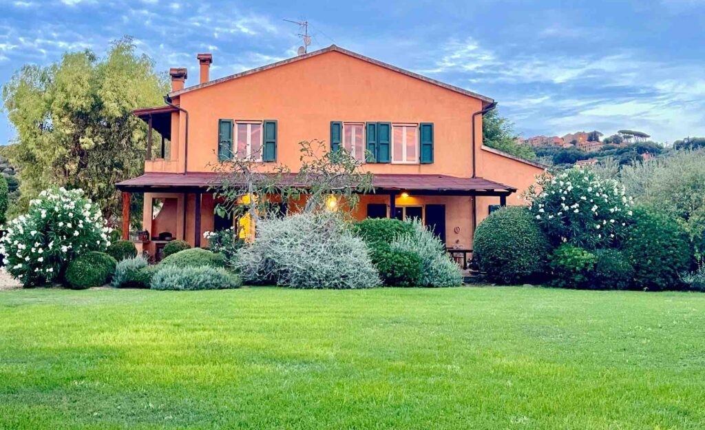 Orange Tuscan farmhouse with green shutters, surrounded by a garden and blue sky