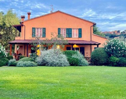 Orange Tuscan farmhouse with green shutters, surrounded by a garden and blue sky