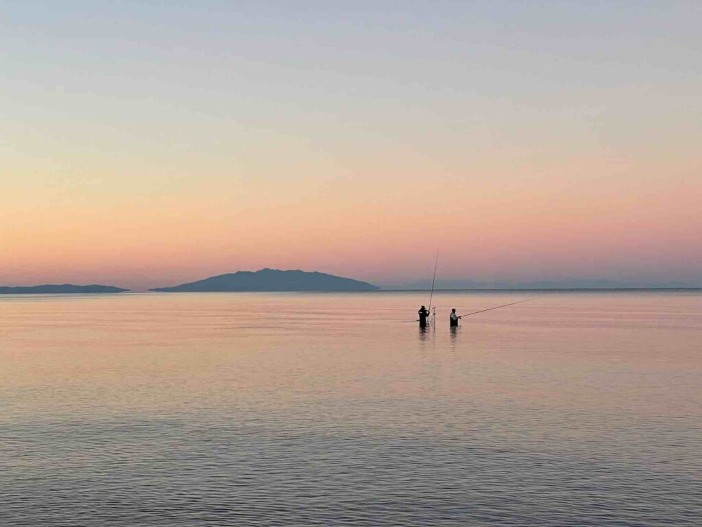 Sunset over the sea with two people fishing from the shallows