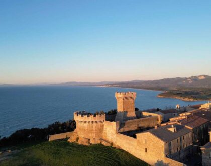 Aerial view of a fortified medieval village on a cliff overlooking the Tyrrhenian Sea along Tuscany's Etruscan Coast at sunset