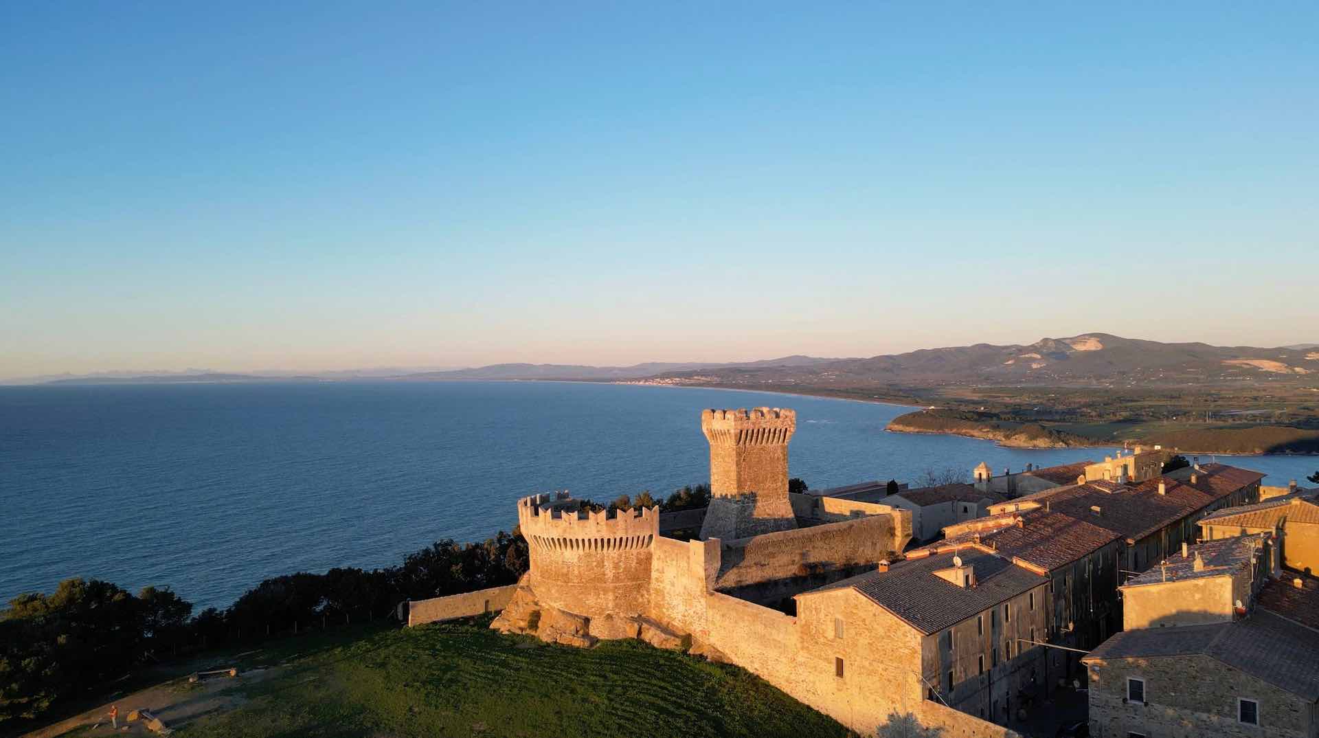 Aerial view of a fortified medieval village on a cliff overlooking the Tyrrhenian Sea along Tuscany's Etruscan Coast at sunset
